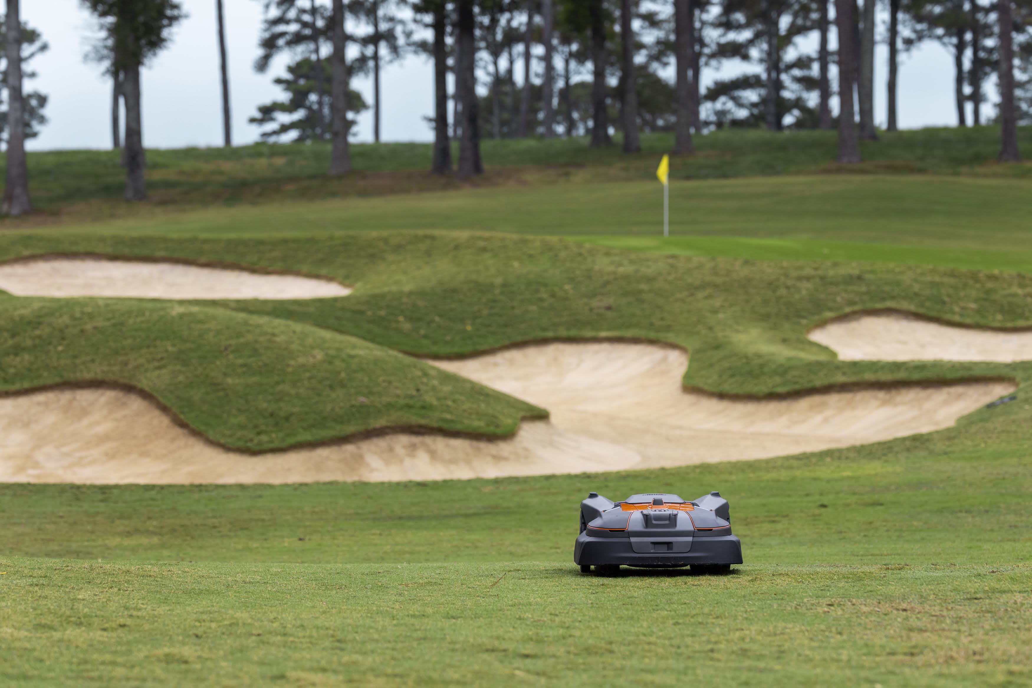 Robotic lawn mower on a golf course fairway near sand bunkers